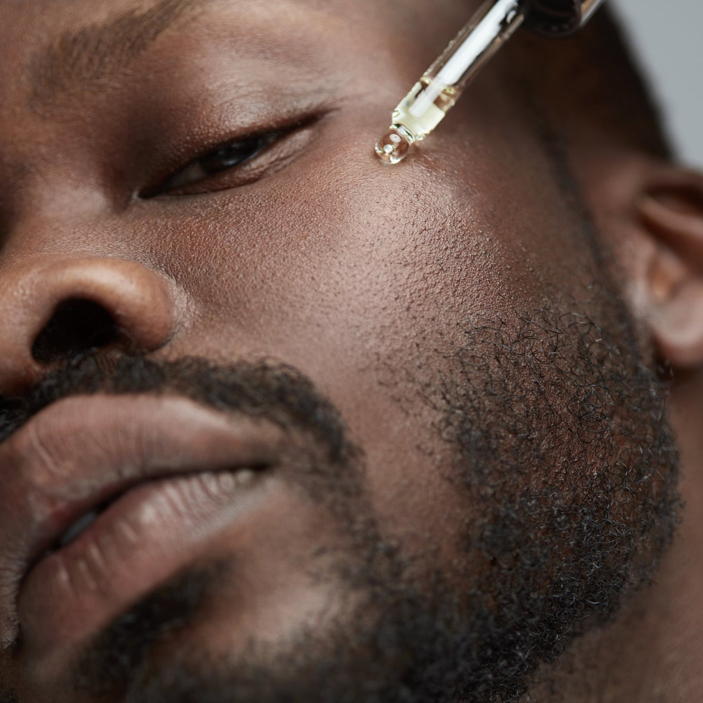 Close-up of a man's face with a dropper applying a substance to his skin.